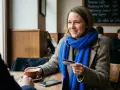 Kobieta z niebieskim szalikiem trzyma kartę płatniczą, zastanawiając się, czy w Norwegii można płacić euro.