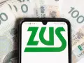 Smartfon z logo ZUS na tle polskich banknotów 100 zł.