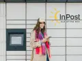 Uśmiechnięta dziewczyna z telefonem w ręku przy paczkomacie InPost. Szybki kurs obsługi, by odebrać przesyłkę.