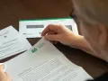 Dłoń starszej osoby przegląda dokumenty z ZUS. W tle koperta z logo ZUS.