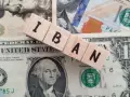 Drewniane klocki z literami IBAN leżą na banknotach dolarowych. Ile cyfr ma numer konta IBAN? To zależy od kraju, ale zazwyczaj jest to 20-34 znaki.