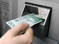 Ręka wkłada banknot 100 zł do bankomatu. Czy państwo może zabrać pieniądze z konta w razie wojny?