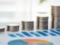 Rosnące stosy monet na wykresie symbolizują walkę z deficytem budżetowym i dążenie do stabilności finansowej.