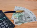 Kalkulator, długopis i banknoty 100 zł. Szukasz, który bank ma najwyższe oprocentowanie lokat na 3 miesiące?