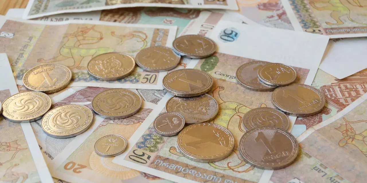 Monety i banknoty, w tym waluta Gruzji, lari, leżą rozrzucone na stole.