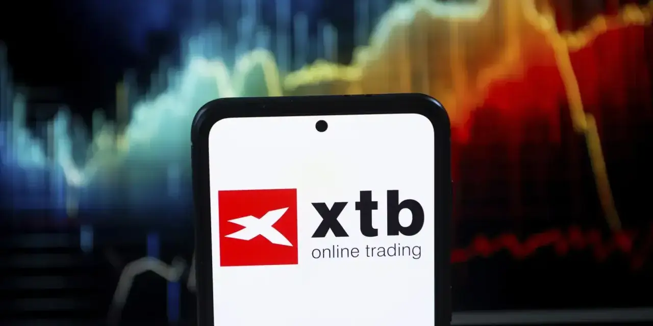 Telefon z logo XTB online trading na tle wykresu giełdowego. Czy XTB jest bezpieczne? Analiza rynku.