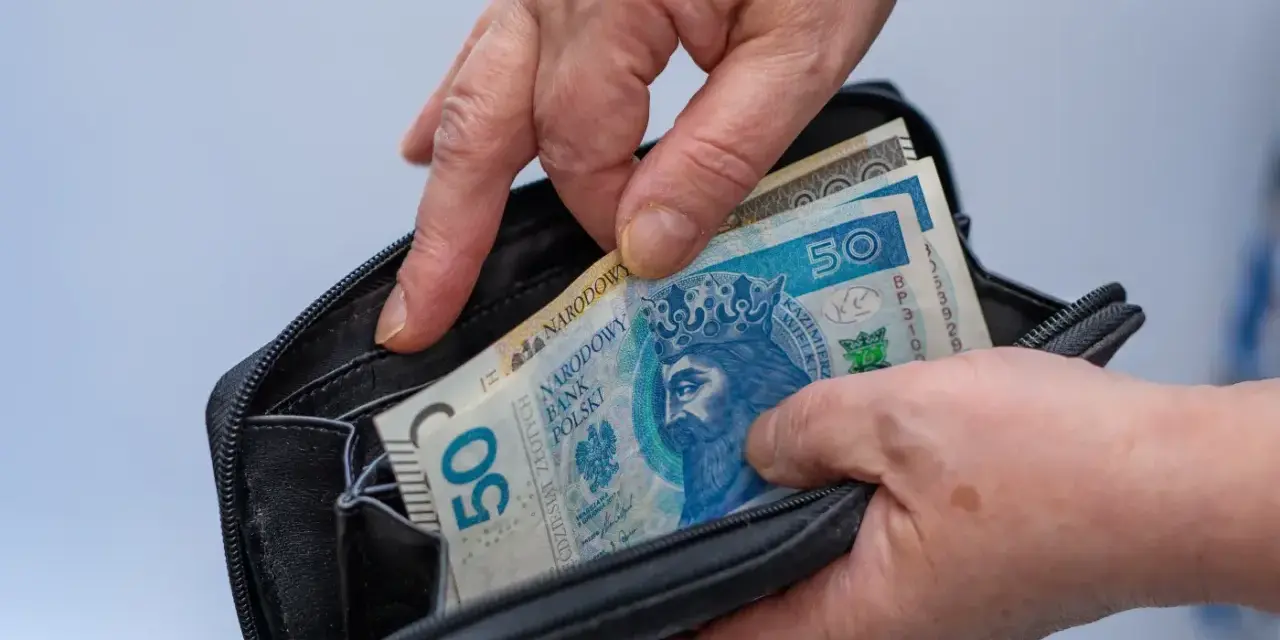 Ręce wkładają polskie banknoty 50 zł do portfela. Czy mam 58 lat i mogę przejść na emeryturę?