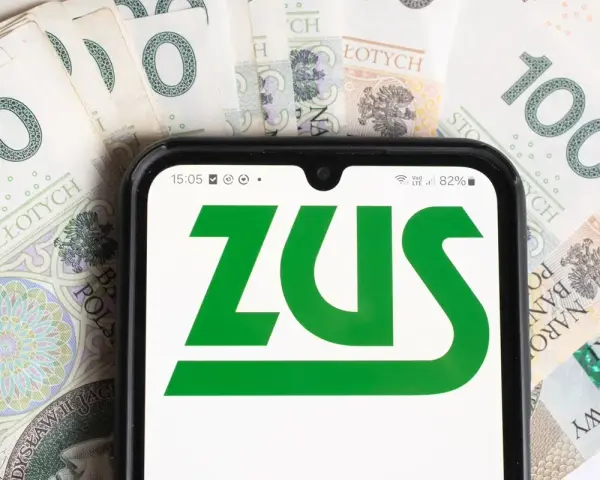 Smartfon z logo ZUS na tle polskich banknotów 100 zł.