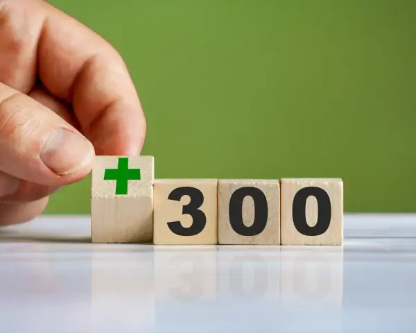 Dłoń układa kostkę z zielonym plusem obok kostek z napisem "300". To dobry start dla kogoś, kto chce zacząć coś nowego.