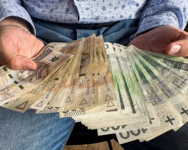Ręce trzymające plik banknotów 100, 200 i 500 zł. Zastanawiasz się, do jakiej kwoty można zrobić przelew bez podatku?