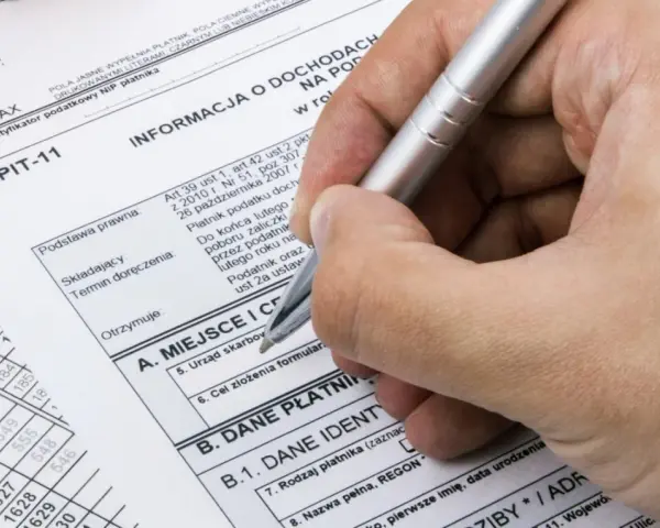 Dłoń z długopisem wypełnia formularz PIT-11. To ważny dokument podatkowy.
