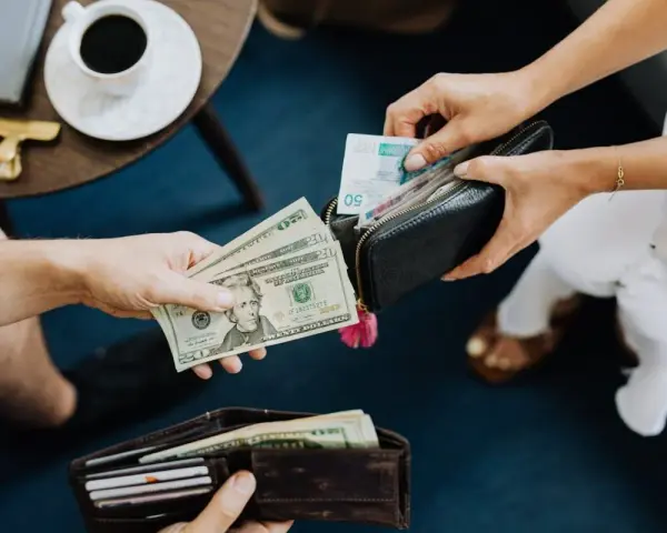 Dłonie przekazują sobie pieniądze. Jedna osoba daje banknoty dolarowe, druga wyciąga z portfela polskie złotówki. To jak wymiana walut, gdzie każda lira ma znaczenie.
