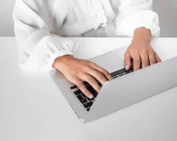 Osoba w białej koszuli pisze na laptopie, przygotowując zaświadczenie o niezaleganiu ZUS.