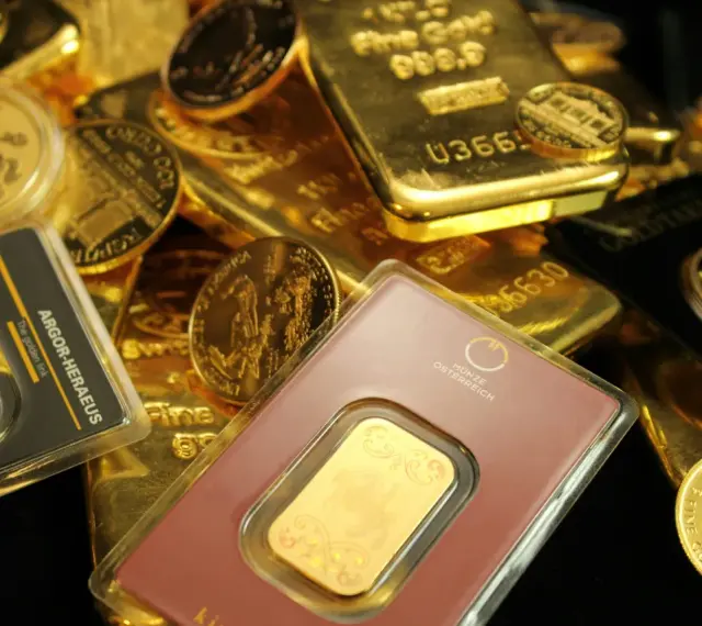 Złote sztabki i monety, w tym gram złota w opakowaniu z napisem "The golden link".