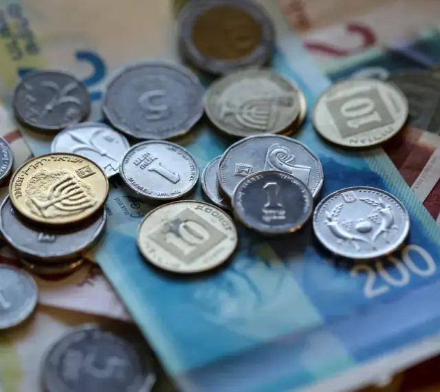 Stos monet i banknotów, w tym szekla, tworzy bogactwo na stole.