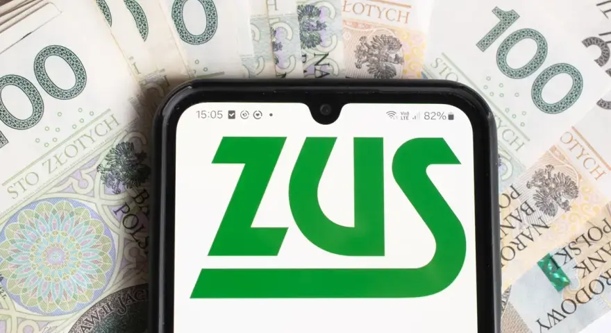 Smartfon z logo ZUS na tle polskich banknotów 100 zł.