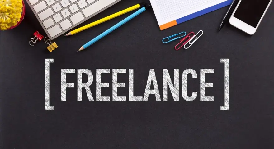 Biurko z klawiaturą, telefonem i napisem "FREELANCE". To styl pracy, gdzie pracujesz dla różnych klientów, sam ustalając godziny.
