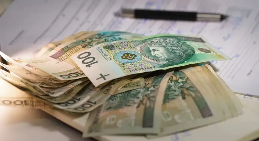 Stos banknotów 100 zł na dokumentach. Czy to wystarczy na najniższą emeryturę?