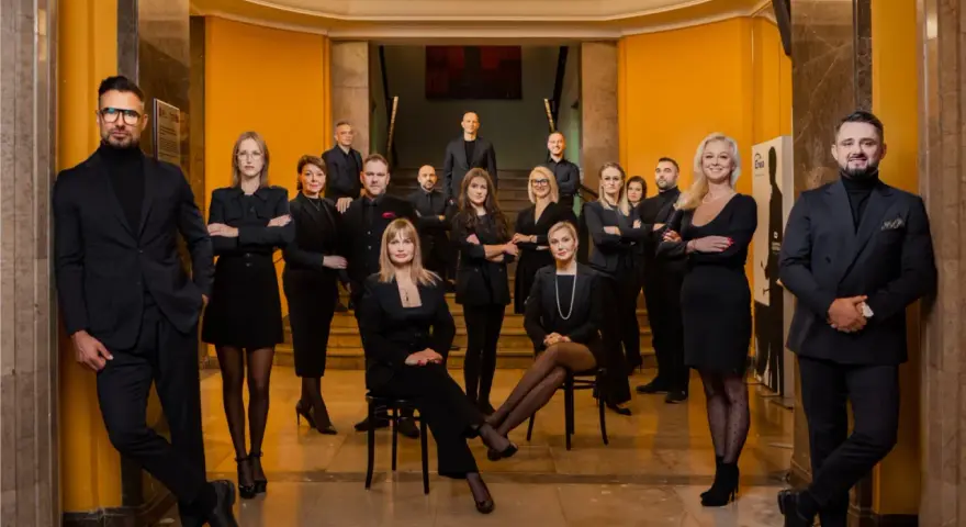 Grupa profesjonalistów w czarnych strojach pozuje w eleganckim wnętrzu.