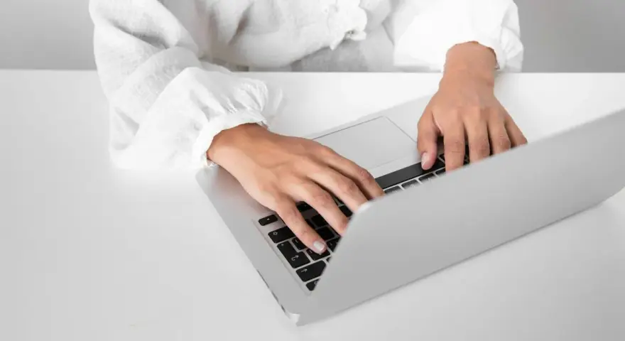Osoba w białej koszuli pisze na laptopie, przygotowując zaświadczenie o niezaleganiu ZUS.
