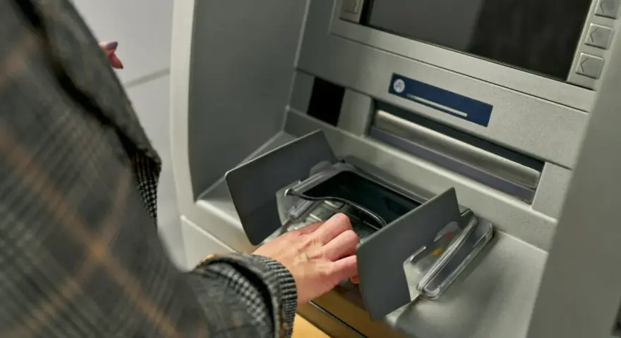 Dłoń w rękawie w kratę wkłada pieniądze do bankomatu. Szybka jednorazowa wpłata gotówki do banku.