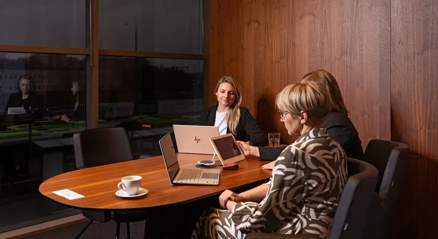 Trzy kobiety omawiają strategię w nowoczesnym biurze. Dyskretne spotkanie, które może dotyczyć usług private banking.