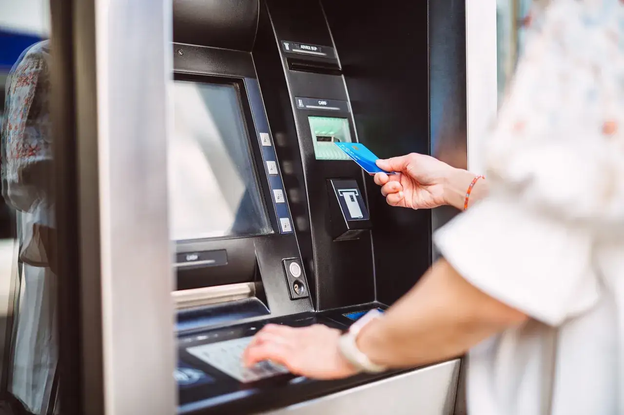 Kobieta wkłada kartę do bankomatu, przygotowując się, jak wpłacić pieniądze na konto. Wpisuje PIN na klawiaturze.
