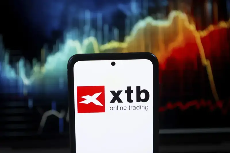 Telefon z logo XTB online trading na tle wykresu giełdowego. Czy XTB jest bezpieczne? Analiza rynku.