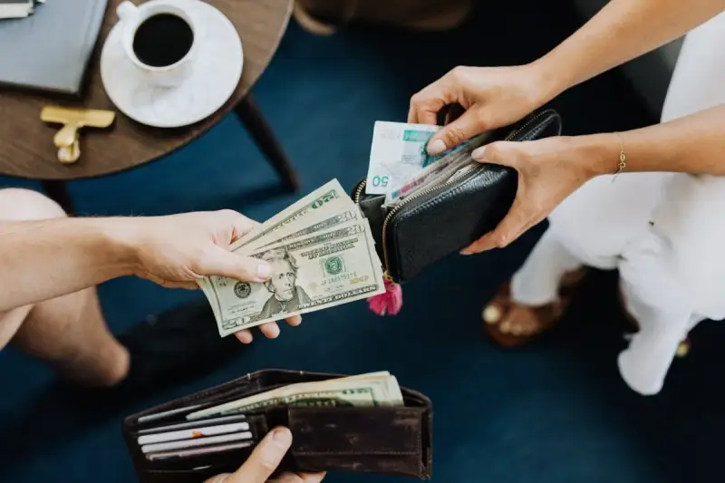 Dłonie przekazują sobie pieniądze. Jedna osoba daje banknoty dolarowe, druga wyciąga z portfela polskie złotówki. To jak wymiana walut, gdzie każda lira ma znaczenie.